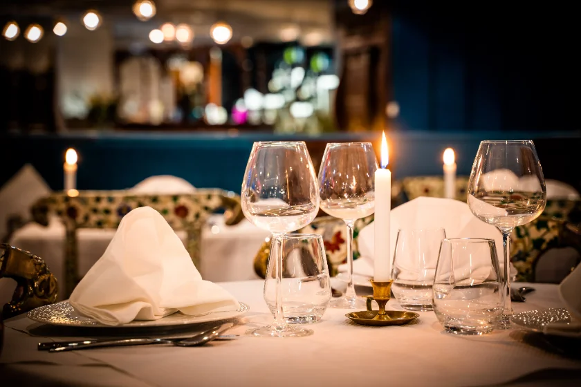 Photographie corporate et architecture d'intérieur pour un restaurant gastronomique à Paris. Gros plan cinématographique en basse lumière sur des verres en cristal, des serviettes blanches pliées et une bougie allumée lors d'un dîner d'affaires.